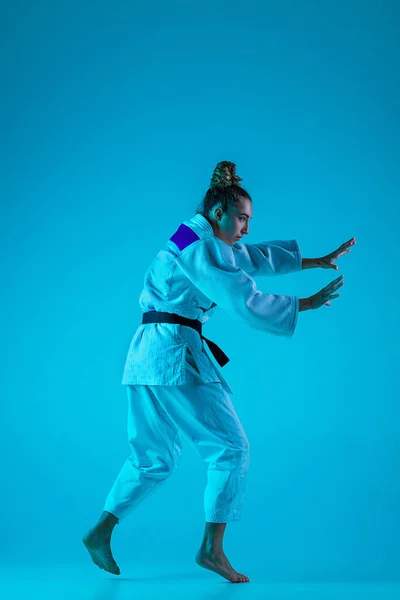 Jonge meisje professionele judoist geïsoleerd op blauwe studio achtergrond in neon licht. Gezonde levensstijl, sportconcept. — Stockfoto