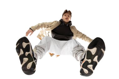 Modern sokak tarzı kıyafetli genç bir adam beyaz arka planda izole edilmiş, alttan vurulmuş.