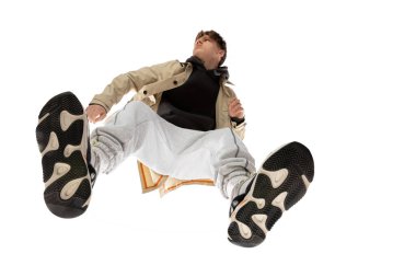 Modern sokak tarzı kıyafetli genç bir adam beyaz arka planda izole edilmiş, alttan vurulmuş.