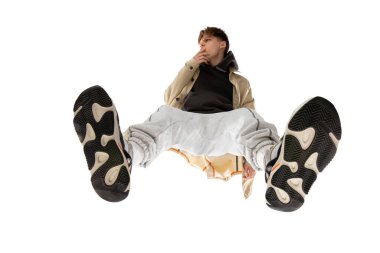 Modern sokak tarzı kıyafetli genç bir adam beyaz arka planda izole edilmiş, alttan vurulmuş.