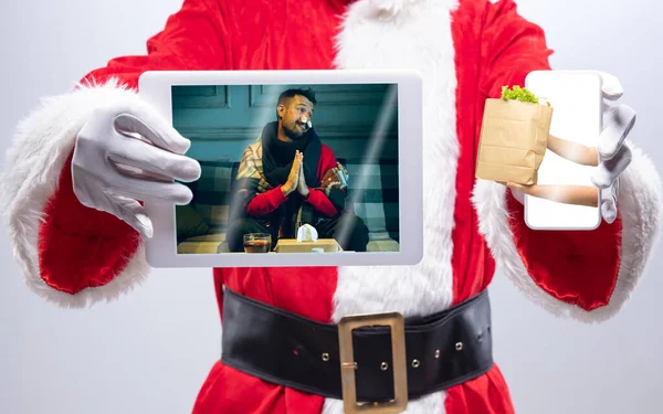 Fechar as mãos do Papai Noel segurando dispositivo com as mãos dando comida para o homem doente na tela — Fotografia de Stock