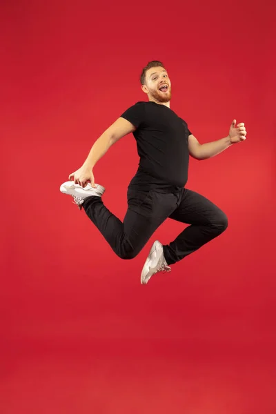 Full length portrait of young successfull high jumping man gesturing isolated on red studio background — Stock Photo, Image