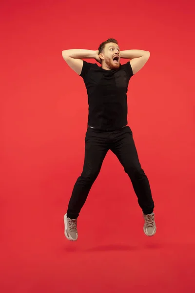 Full length portrait of young successfull high jumping man gesturing isolated on red studio background — 스톡 사진