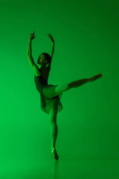 Joven y elegante bailarina de ballet aislada sobre fondo de estudio verde degradado en luz de neón. Arte en movimiento — Foto de Stock