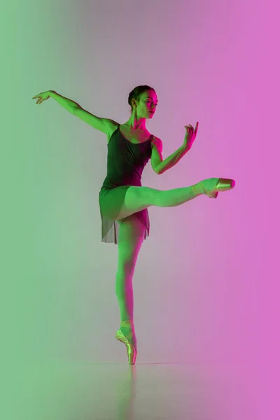 Joven y elegante bailarina de ballet aislada en el fondo del estudio de color rosa verdoso degradado en luz de neón. Arte en movimiento — Foto de Stock