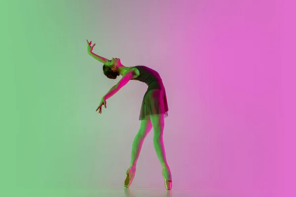 Młoda i pełna wdzięku tancerka baletowa odizolowana na gradientowym różowo-zielonym tle studia w neonowym świetle. Sztuka w ruchu — Zdjęcie stockowe