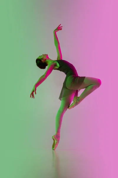 Fiatal és kecses balett táncos elszigetelt gradiens rózsaszín-zöld stúdió háttér neon fényben. Mozgásban lévő művészet — Stock Fotó
