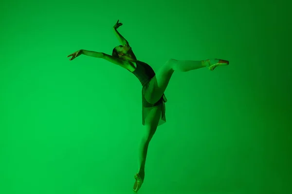 Giovane e graziosa ballerina isolata su uno sfondo verde sfumato da studio in luce al neon. Arte in movimento — Foto Stock