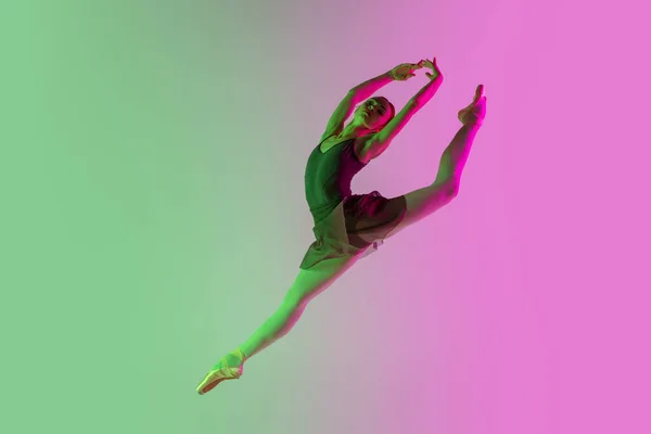Молодая и изящная балетная танцовщица выделена на градиентном розово-зеленом фоне студии в неоновом свете. Искусство в действии — стоковое фото