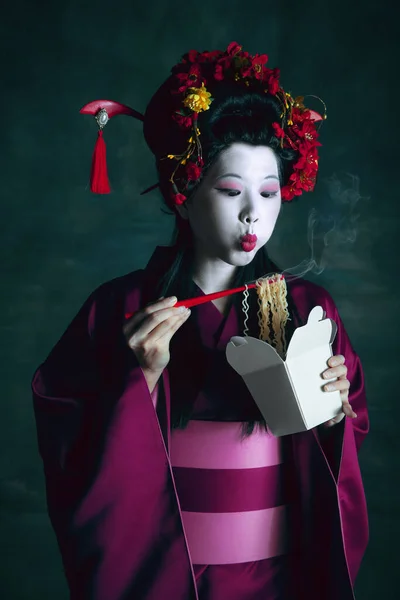 Fiatal japán nő, mint gésa, sötétzöld háttérrel. Retro stílus, a korszakok fogalmának összehasonlítása. — Stock Fotó