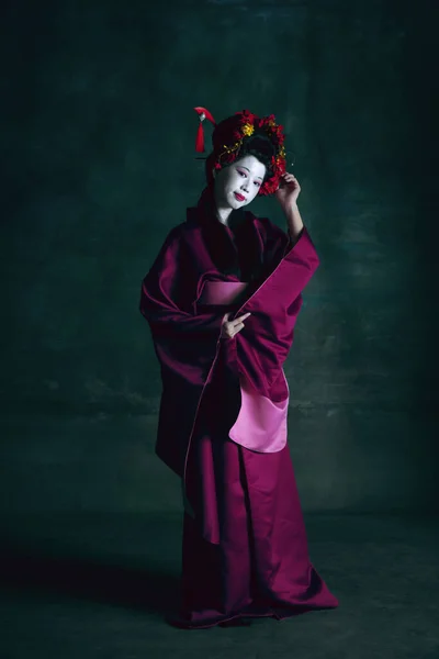 Ung japansk kvinna som geisha på mörkgrön bakgrund. Retrostil, jämförelse av tidsepoker koncept. — Stockfoto