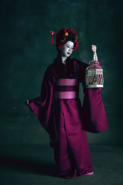 Ung japansk kvinna som geisha på mörkgrön bakgrund. Retrostil, jämförelse av tidsepoker koncept. — Stockfoto