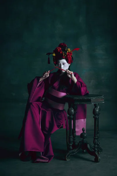 Jonge Japanse vrouw als geisha op donkergroene achtergrond. Retro stijl, vergelijking van tijdperken concept. — Stockfoto