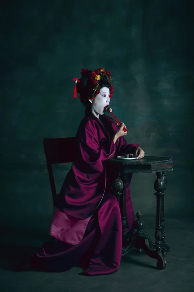 Fiatal japán nő, mint gésa, sötétzöld háttérrel. Retro stílus, a korszakok fogalmának összehasonlítása. — Stock Fotó