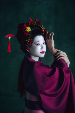 Koyu yeşil arka planda geyşa gibi genç Japon kadın. Retro biçimi, dönemin karşılaştırması.
