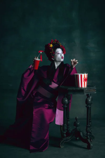 Jonge Japanse vrouw als geisha op donkergroene achtergrond. Retro stijl, vergelijking van tijdperken concept. — Stockfoto