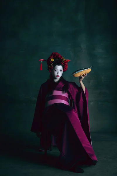 Jovem mulher japonesa como gueixa no fundo verde escuro. Estilo retro, comparação do conceito eras. — Fotografia de Stock