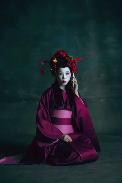 Jovem mulher japonesa como gueixa no fundo verde escuro. Estilo retro, comparação do conceito eras. — Fotografia de Stock