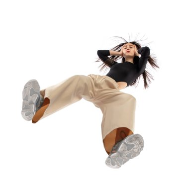 Modern sokak tarzı kıyafetli genç bir kadın beyaz arka planda izole edilmiş, alttan vurulmuş.