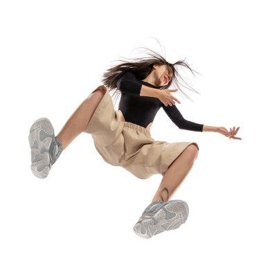 Modern sokak tarzı kıyafetli genç bir kadın beyaz arka planda izole edilmiş, alttan vurulmuş.