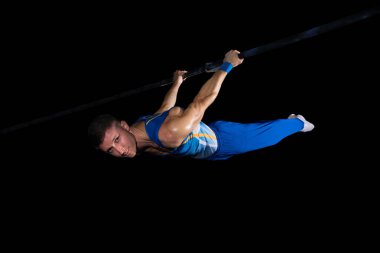 Spor salonunda kaslı erkek jimnastikçi, esnek ve aktif. Kafkasyalı formda bir adam, mavi spor giyimli bir atlet, siyahta izole edilmiş.