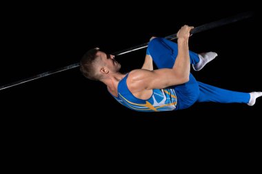 Spor salonunda kaslı erkek jimnastikçi, esnek ve aktif. Kafkasyalı formda bir adam, mavi spor giyimli bir atlet, siyahta izole edilmiş.