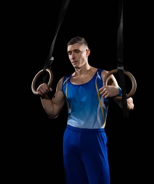 Muscular male gymnast training in gym, flexible and active. Caucasian fit guy, athlete in blue sportswear isolated on black
