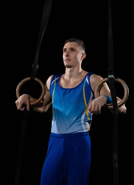 Treinamento de ginasta masculino muscular em ginásio, flexível e ativo. Caucasiano em forma cara, atleta de sportswear azul isolado em preto — Fotografia de Stock