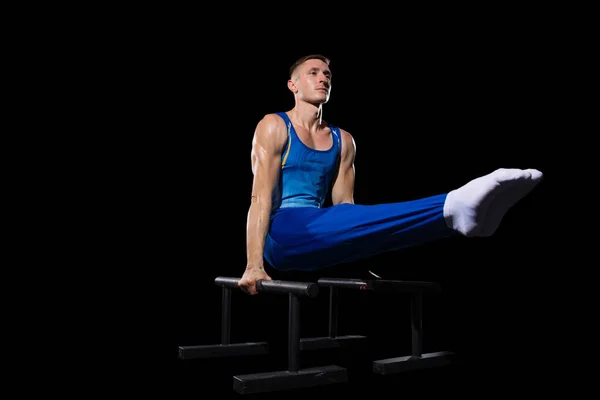 Entrenamiento muscular masculino de gimnasta en gimnasio, flexible y activo. Caucásico chico en forma, atleta en ropa deportiva azul aislado en negro — Foto de Stock