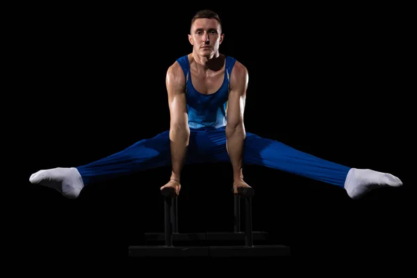 Мышечная мужская гимнастика в тренажерном зале, гибкая и активная. Белый парень, спортсмен в синей спортивной одежде, изолированный на черном — стоковое фото
