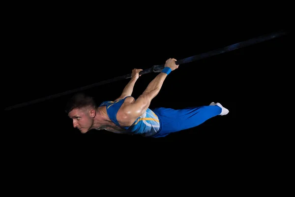 Treinamento de ginasta masculino muscular em ginásio, flexível e ativo. Caucasiano em forma cara, atleta de sportswear azul isolado em preto — Fotografia de Stock