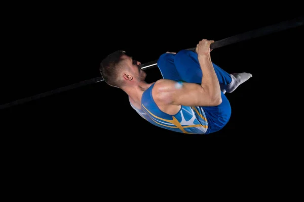 Muscular male gymnast training in gym, flexible and active. Caucasian fit guy, athlete in blue sportswear isolated on black