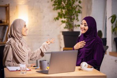 Ders sırasında evde oturup bilgisayar başında eğitim gören mutlu iki Müslüman kadın.