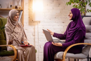 Ders sırasında evde oturup bilgisayar başında eğitim gören mutlu iki Müslüman kadın.