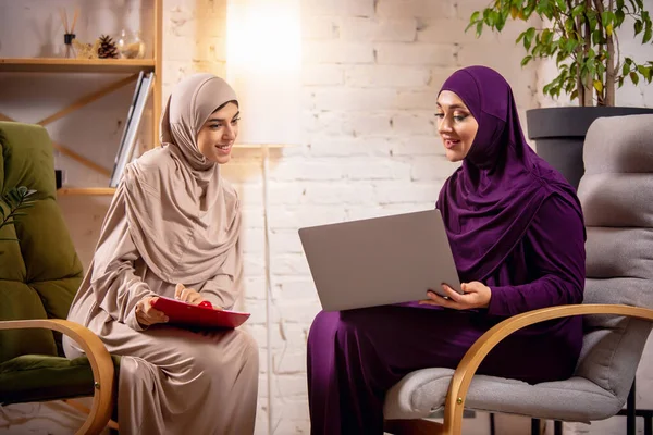 Happy two muslim women at home during lesson, studying near computer, online education