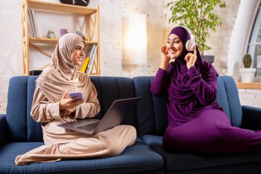 Mutlu iki Müslüman kadın evde konuşuyor, gülümsüyor, eğleniyor. Arkadaşlık, modern teknoloji, duygu kavramı.