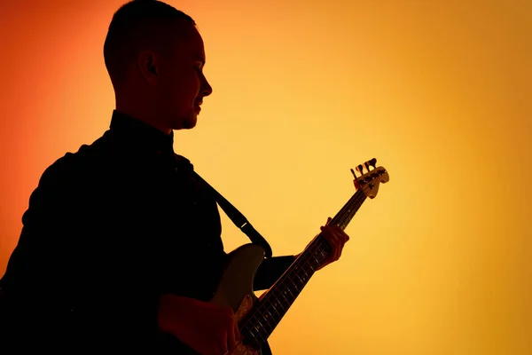 霓虹灯下橙色渐变演播室背景中孤立的年轻高加索男性吉他手的轮廓 — 图库照片