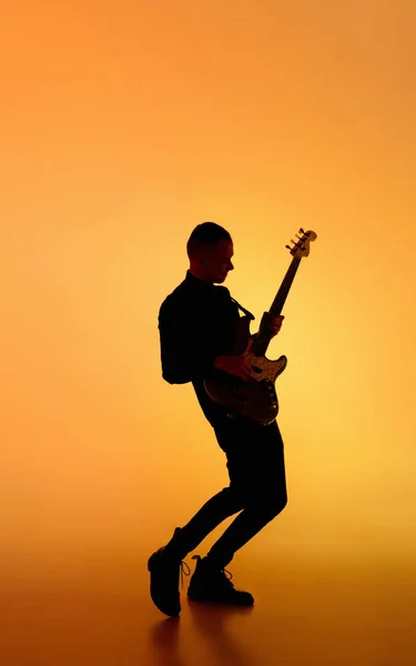 Silhueta de jovem guitarrista masculino caucasiano isolado em fundo estúdio gradiente laranja em luz de néon — Fotografia de Stock