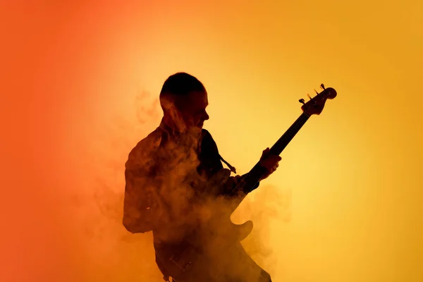 Silhueta de jovem guitarrista masculino caucasiano isolado em fundo estúdio gradiente laranja em luz de néon — Fotografia de Stock