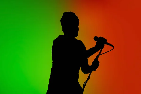 Sylwetka młodego białego wokalisty odizolowanego na zielono-pomarańczowym tle studia gradientowego w świetle neonowym — Zdjęcie stockowe