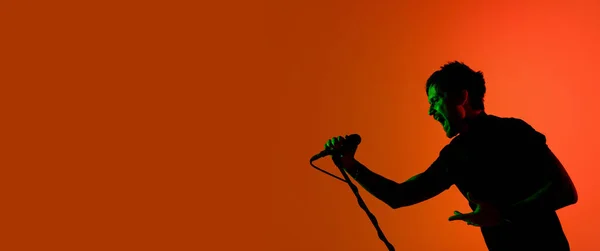 Sylwetka młodego białego wokalisty odizolowanego na pomarańczowym tle studia gradientowego w świetle neonowym — Zdjęcie stockowe