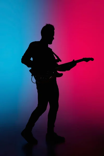 若い白人男性ギタリストのシルエットがネオンライトで青ピンクのグラデーションスタジオの背景に孤立 — ストック写真