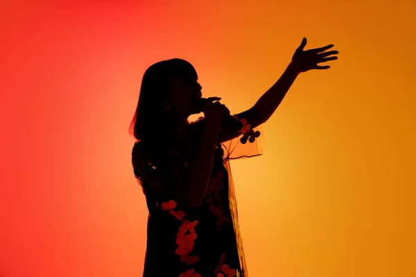 Silhouette of young caucasian female singer isolated on orange gradient studio background in neon light — Stock Photo, Image