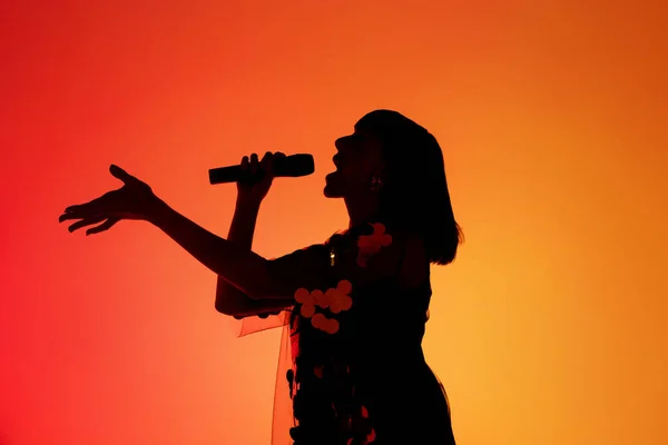 霓虹灯下橙色渐变演播室背景中孤立的年轻高加索女歌手的轮廓 — 图库照片