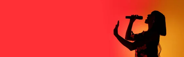 Silhouette di giovane cantante caucasica isolata su sfondo arancione gradiente studio in luce al neon — Foto Stock