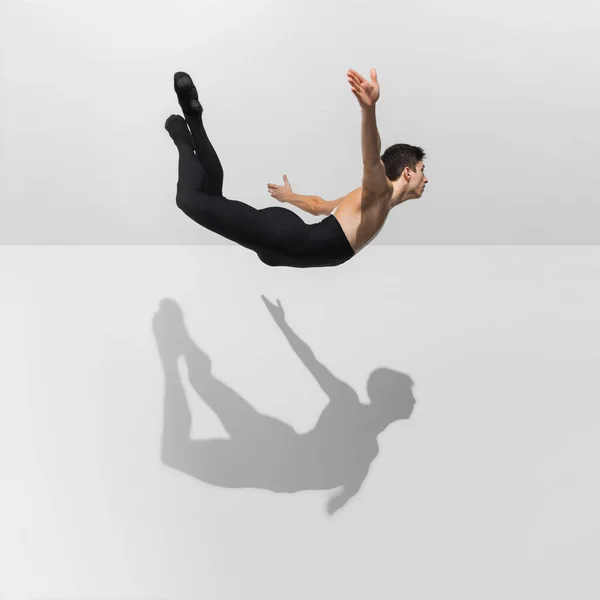 Bonito jovem atleta masculino praticando no fundo do estúdio branco com sombras no salto, voar ar — Fotografia de Stock