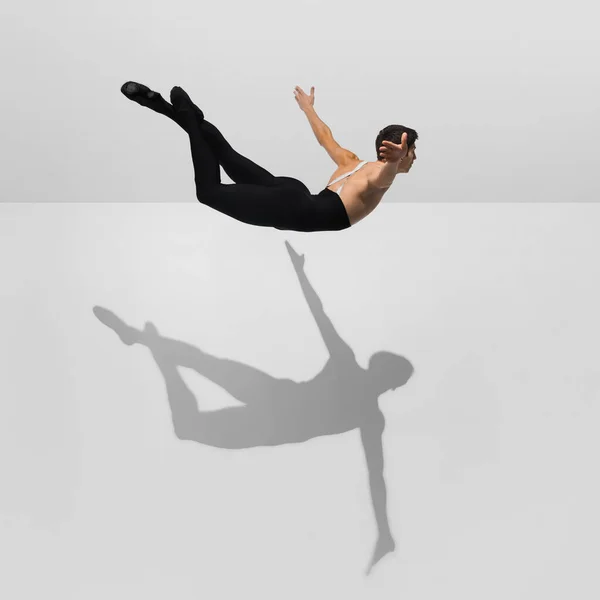 Hermoso joven atleta masculino practicando en fondo blanco estudio con sombras en salto, vuelo aéreo — Foto de Stock