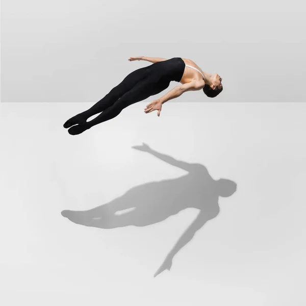 Hermoso joven atleta masculino practicando en fondo blanco estudio con sombras en salto, vuelo aéreo — Foto de Stock