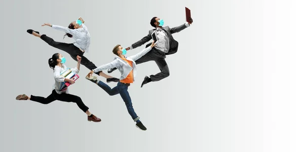 Happy office workers in face masks jumping and dancing in casual clothes or suit isolated on studio background. Creative collage.