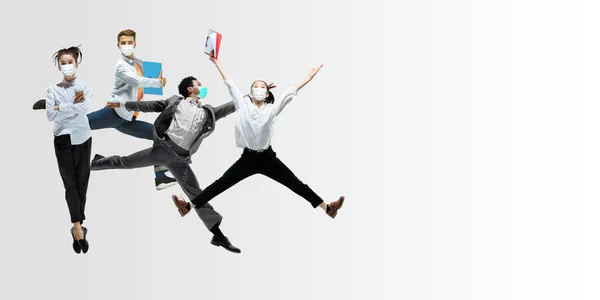 Happy office workers in face masks jumping and dancing in casual clothes or suit isolated on studio background. Creative collage. — Stock Photo, Image